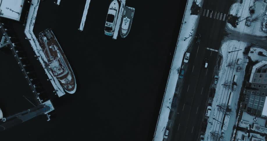 Top down view of a car driving on a street in the city covered in snow next to a marina