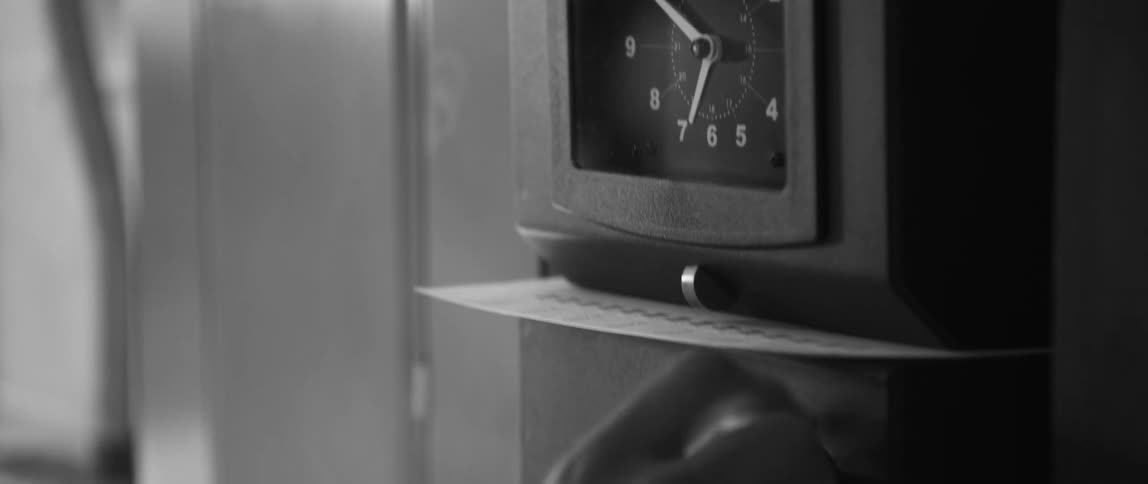 A worker places a time card in a clock card machine and pulls the level before removing the card