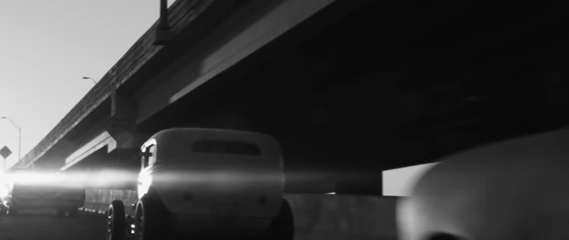 Vintage vehicles move along highway paralleling elevated roadway