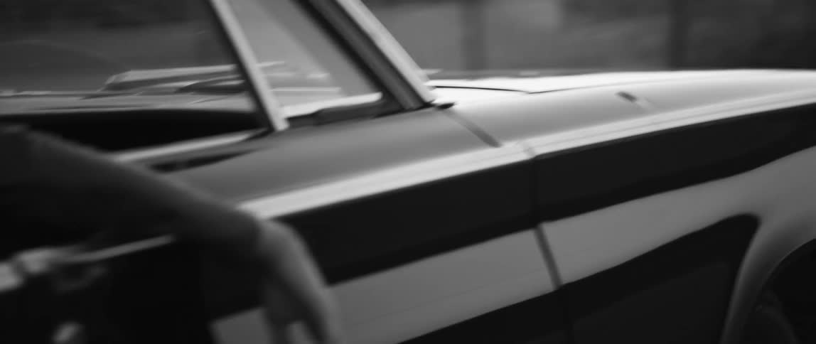 Vintage car drives pass fences as someone hangs arm out of window
