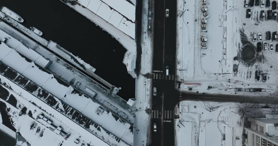 Top down view of vehicles driving on a city street between snow covered buildings