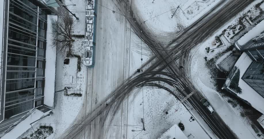 Birds eye descending twist above vehicles and pedestrians crossing a snow covered city intersection