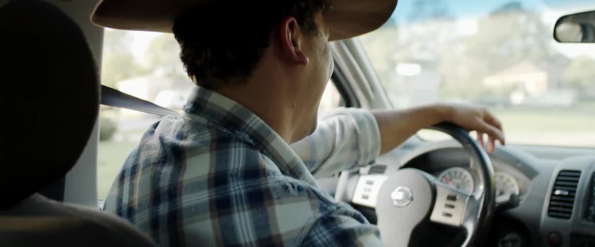 Happy man wearing a cowboy hat driving a car smiles while listening to a woman talking on the passenger seat