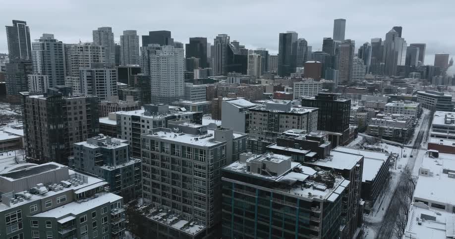 Pullback traverse over buildings in a dense urban area as flurries fall gently from an overcast sky