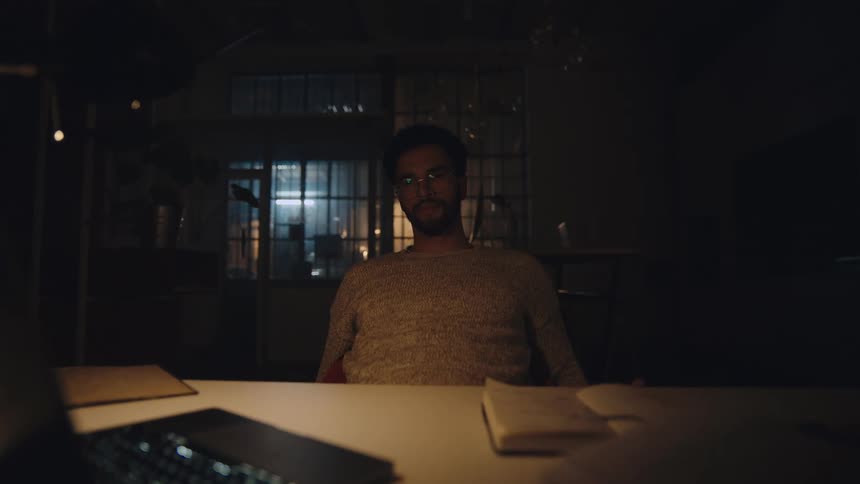 Tired young man sitting at a desk at home stops working on a laptop