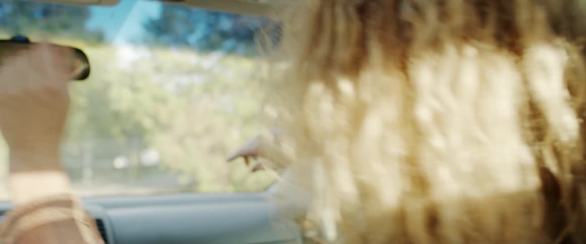 Happy blonde woman shakes her curly hair while sitting on the passenger car driving at morning