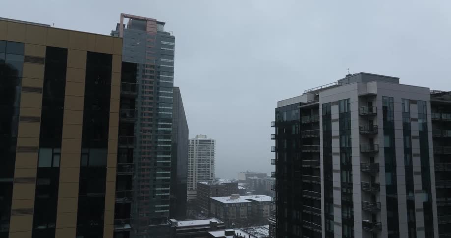 Snow falls between apartment and office buildings in a downtown area