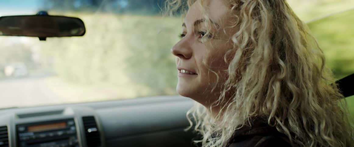 Young happy blonde woman with curly hair sitting on the passenger seat of a driving car talking