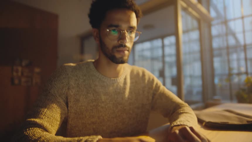 Man sits at table typing on laptop in industrial design room