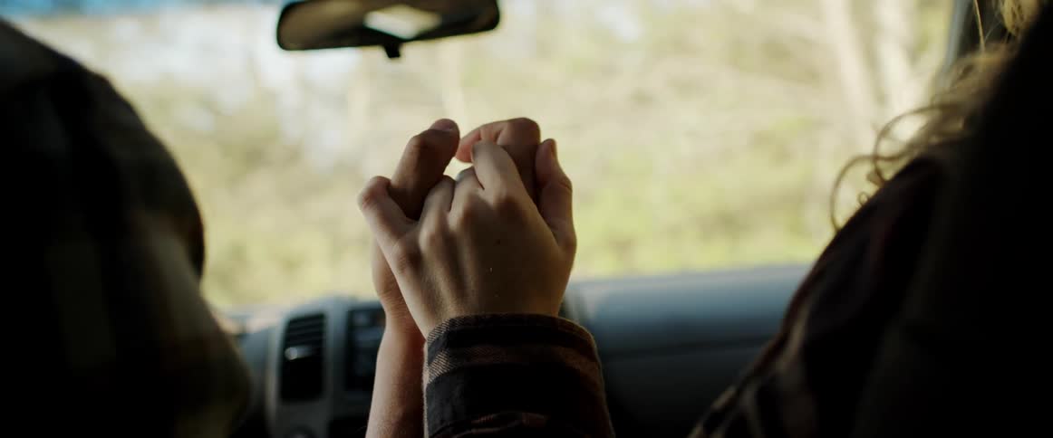 A man and woman hold hands as they drive in a car