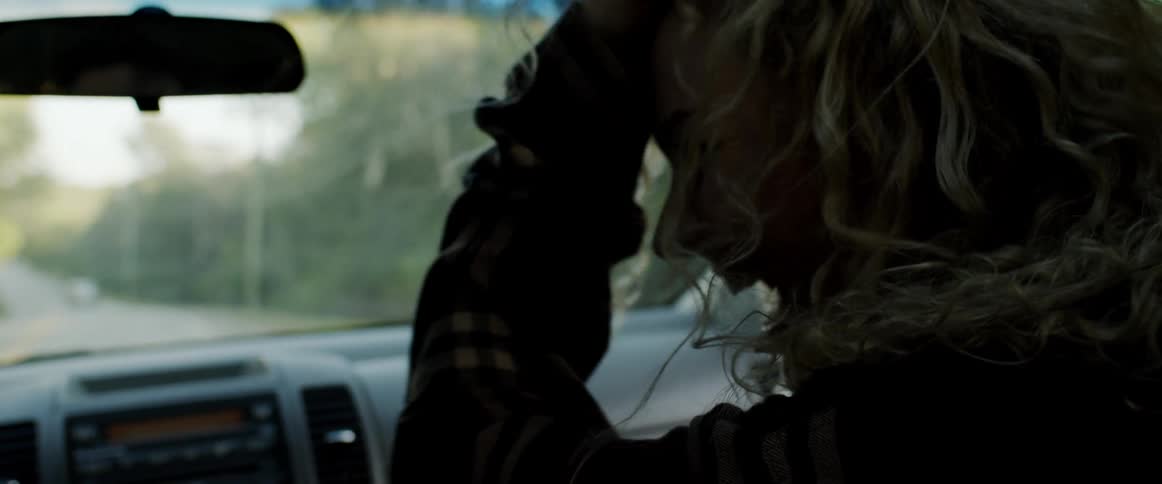 Blonde female passenger in a car smiles and pushes her hair off of her face with her hand on a sunny day