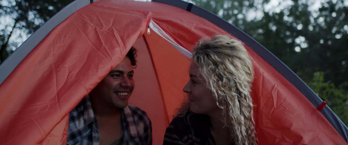 A man and woman talk with one another while sitting in a tent outdoors during the day