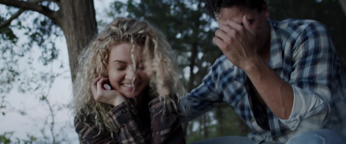 Young couple talking and laughing while sitting on the forest floor at morning