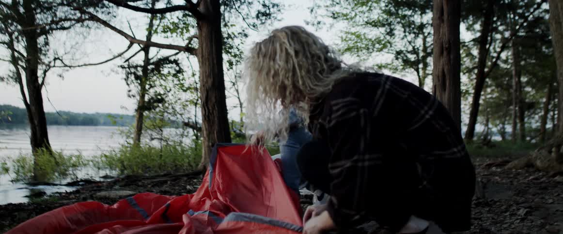 Man and woman prepare to erect a tent at a campsite in the forest next to a lake