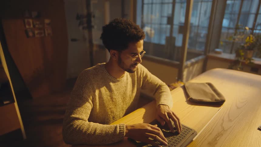 high angle shot of man sitting at a table typing on a laptop computer