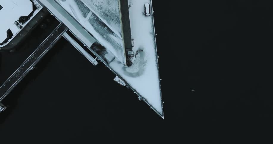 Top down view of a snow covered pier standing above dark and still water