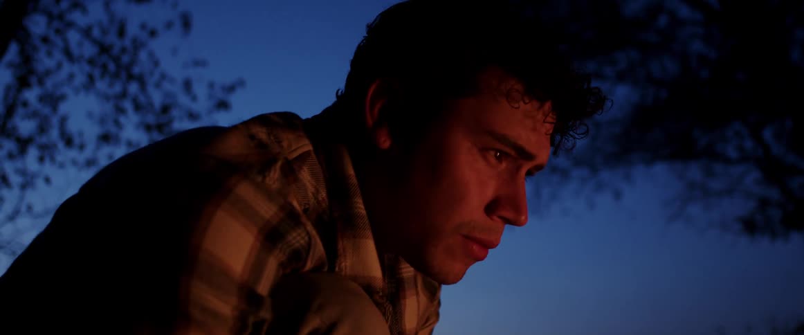 Man gazes into campfire as it casts shadows and light across his face