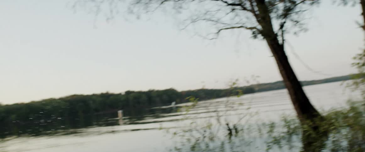Man with a tattoo on his chest stands in the forest and throws a stone into the lake causing ripples in the water