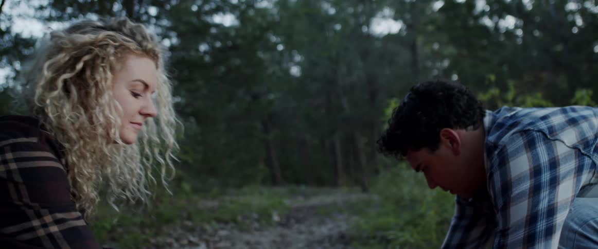 Couple works together crouching in wilderness as they laugh and talk