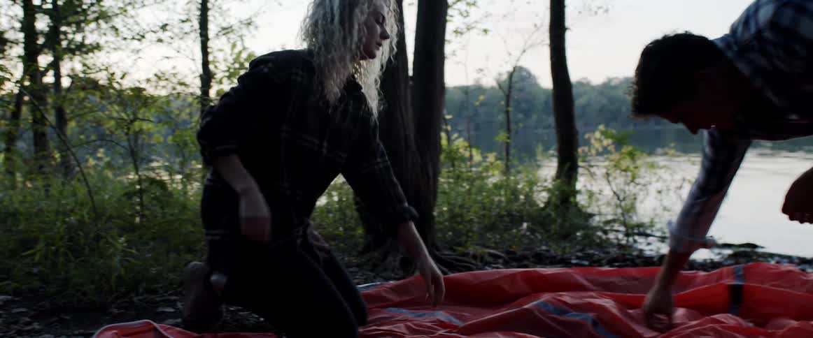 Man and woman setting up a tent in the wilderness near a lake