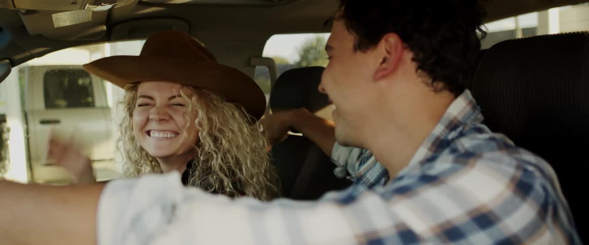 Man puts his hat on womans head as they pull out of gas station