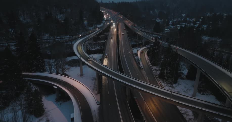 Evening traffic moves along an icy highway interchange as snow falls lightly