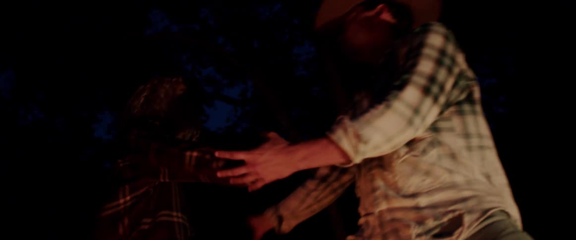 A man and woman dance outside next to a fire at night