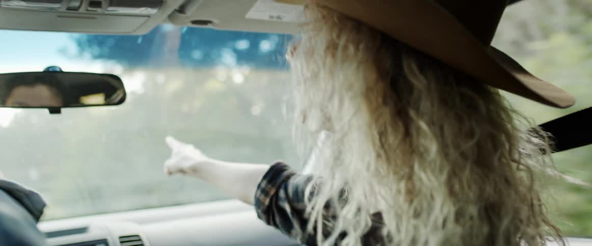 A woman sitting in the passenger seat of a vehicle excitedly points out something further up the road to the driver