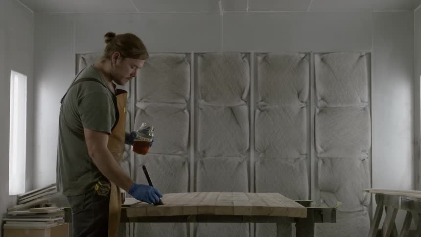 Man applies stain with a brush to a wooden surface