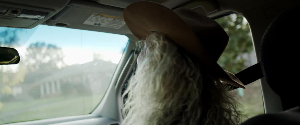 Blonde female passenger wearing a cowboy hat sways in her seat with a smile as the vehicle drives through neighborhood