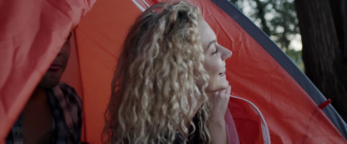 A woman smiles as she looks outside the door of her tent in the woods