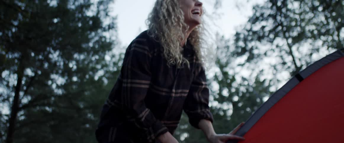 A woman secures a tent while laughing outdoors during the day