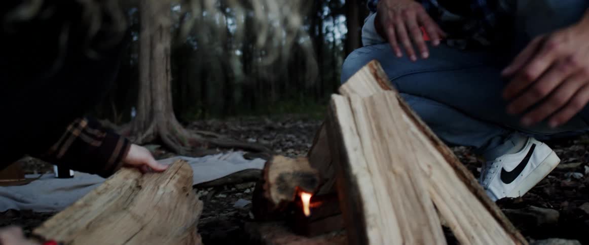 A man and woman try to start a fire while camping in the woods