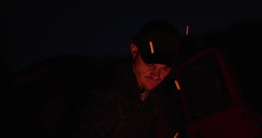 Embers from a campfire swirl around a man at night