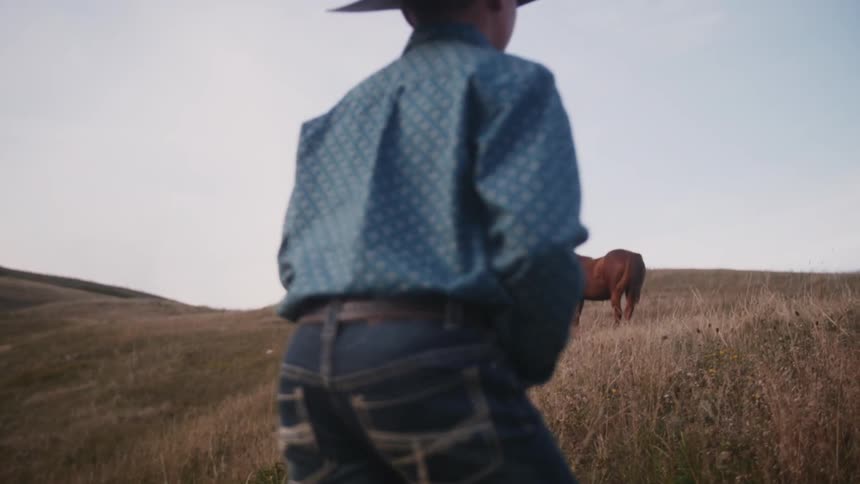 Young cowboy walking up a hill toward some horses