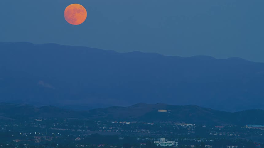 A full moon rises in the sky above a ridge with a town below