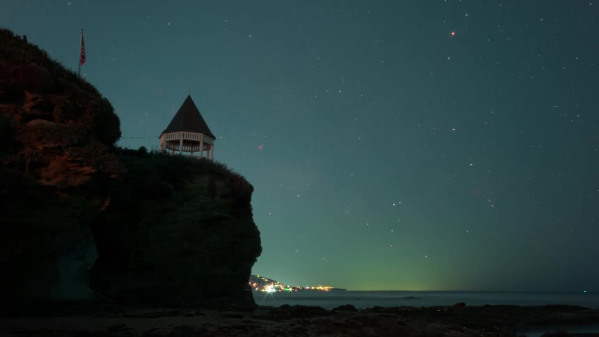 Speed up time lapse of a starry night rolling over a gazebo on a cliff in front of a beach at sunrise