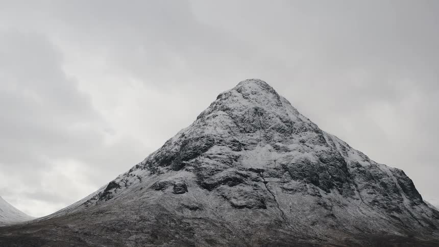 A rocky peak dusted with snow under a gray cloudy sky