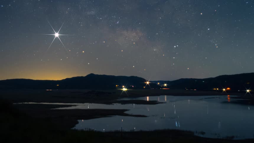 Traffic travels next to the lake at night under a starry sky