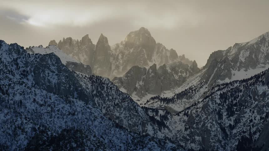 Clouds move over jagged mountains and snow dusted slopes