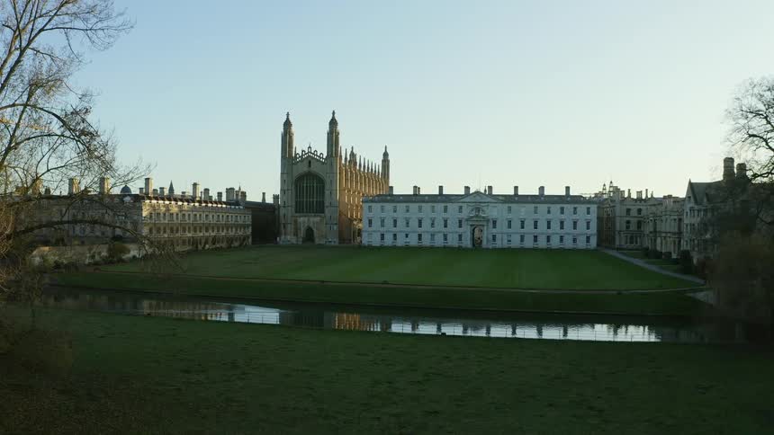 River reflects nearby Kings College Chapel and old world style architecture of nearby buildings under a clear sky