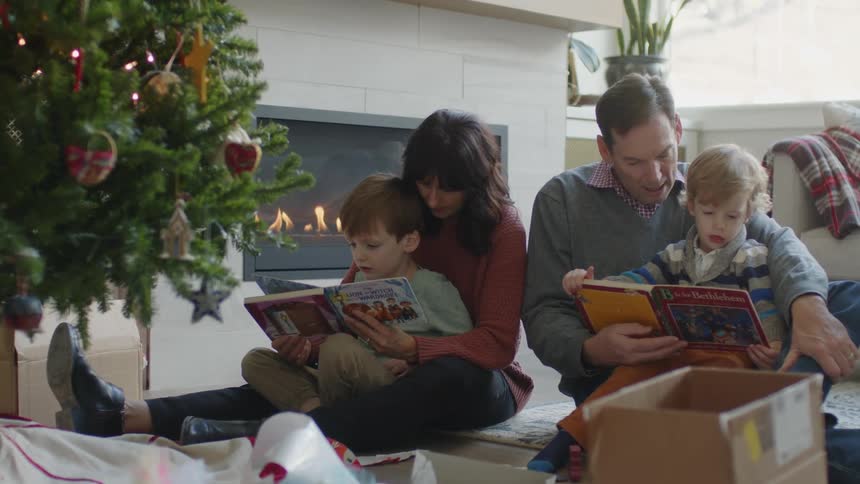 Father and mother read books to sons next to christmas tree and fireplace
