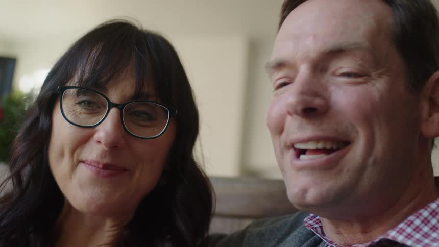 Woman wearing glasses sits next to a man and they both talk and laugh and smile