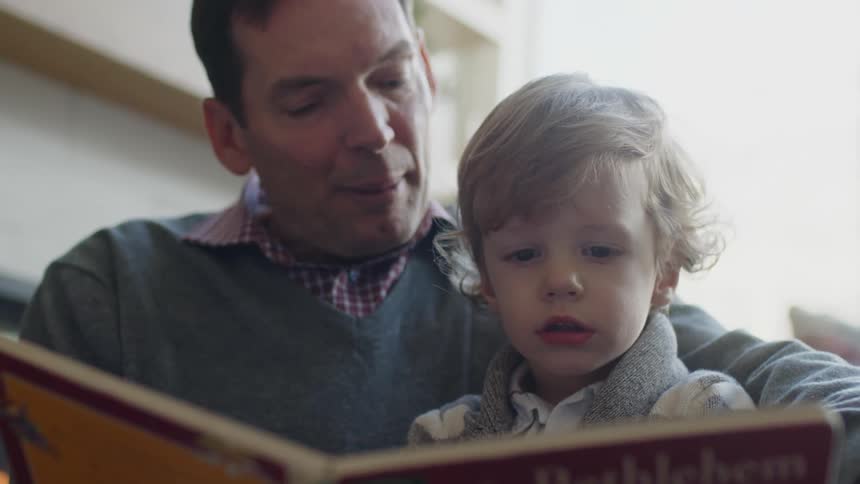 A father reads a book to his son who is sitting on his lap