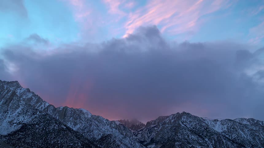 Speed up time lapse of clouds rolling over the snow covered slopes of a mountain range at sunset