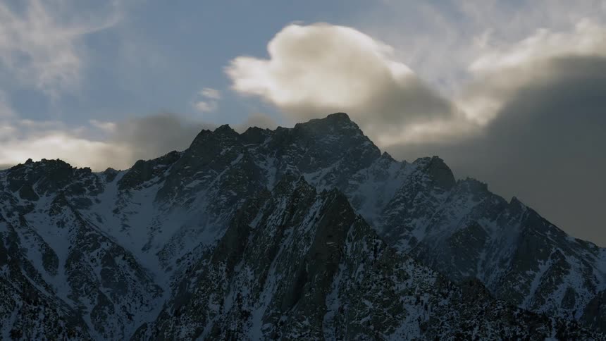 Clouds pass over a snowy mountain during the day