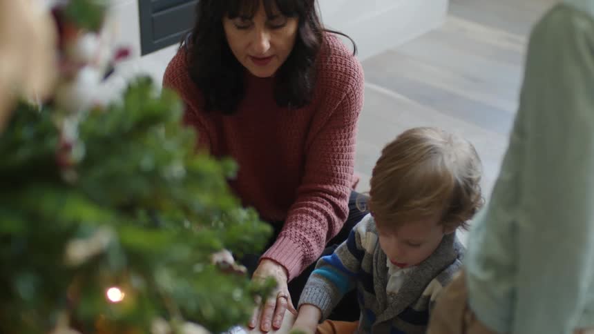 Mother and son opening presents under the christmas tree in front of the chimney in the living room