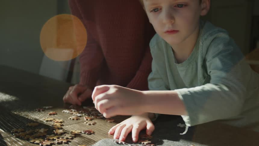 A mother watches as her son puts a puzzle together