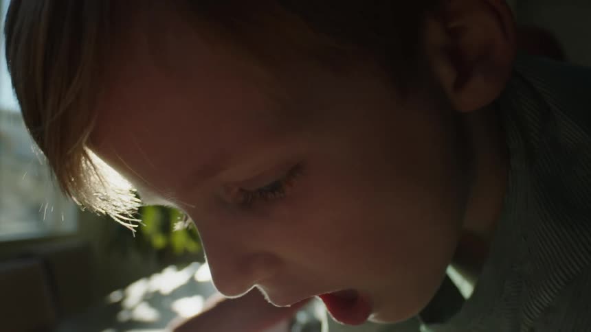 A boy attempts to solve a jigsaw puzzle with his mother indoors during the day