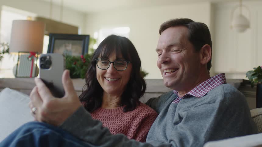 A husband and wife sitting on the couch having a video call with family smiling and joyful